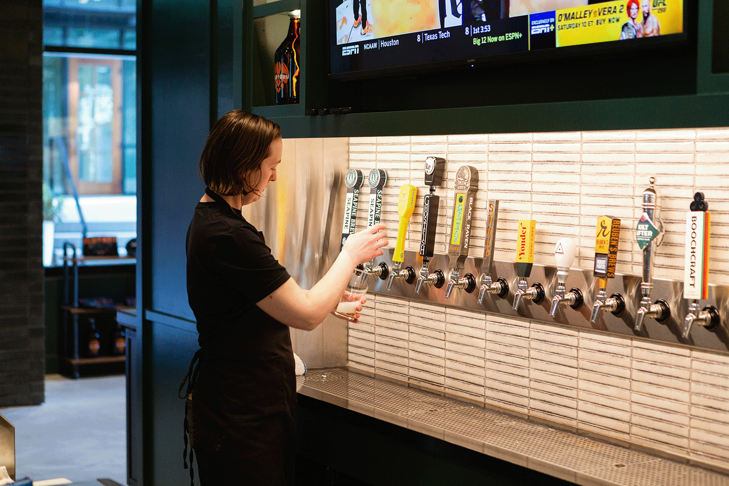 A woman expertly pours a fresh pint from a bar tap lined with a variety of craft beer options
